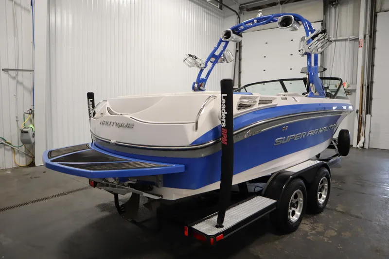 Slide: The Image of 2011 Nautique 210 SUPER AIR boat in a garage, blue and white design, on a trailer. - 5