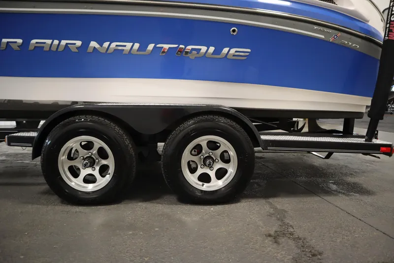 Slide: The Image of 2011 Nautique 210 SUPER AIR boat on trailer, showcasing sleek blue design and dual wheels. - 56