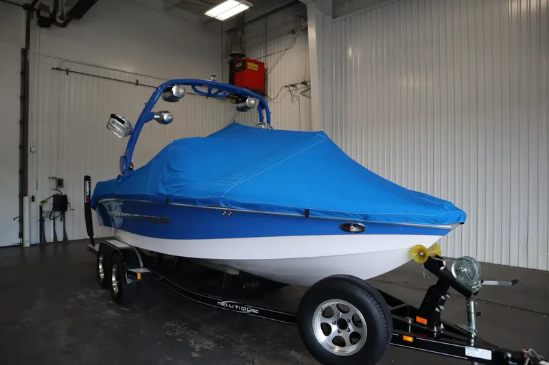 Slide: The Image of 2011 Nautique 210 SUPER AIR boat with blue cover on trailer in garage. - 58