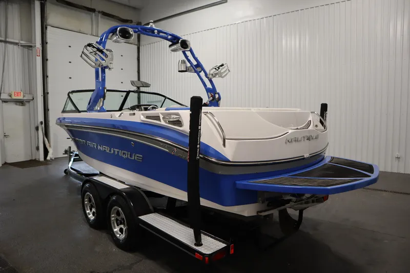 Slide: The Image of 2011 Nautique 210 SUPER AIR boat in a garage, blue and white design, on a trailer. - 7