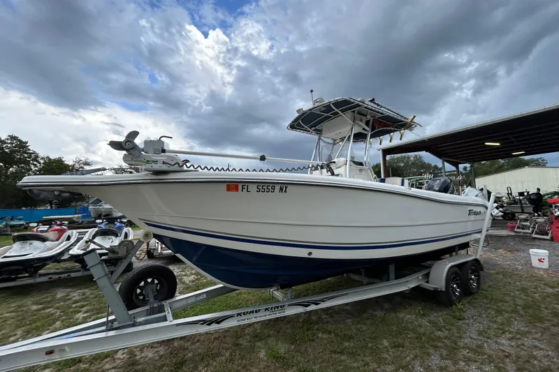 Slide: The Image of 2007 Triton 2486cc boat on trailer under cloudy sky, parked near jet skis. - 3