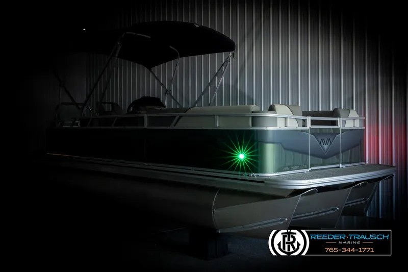 Slide: The Image of 2026 Avalon VEN CRB pontoon boat in dimly lit showroom with green light accent. - 3