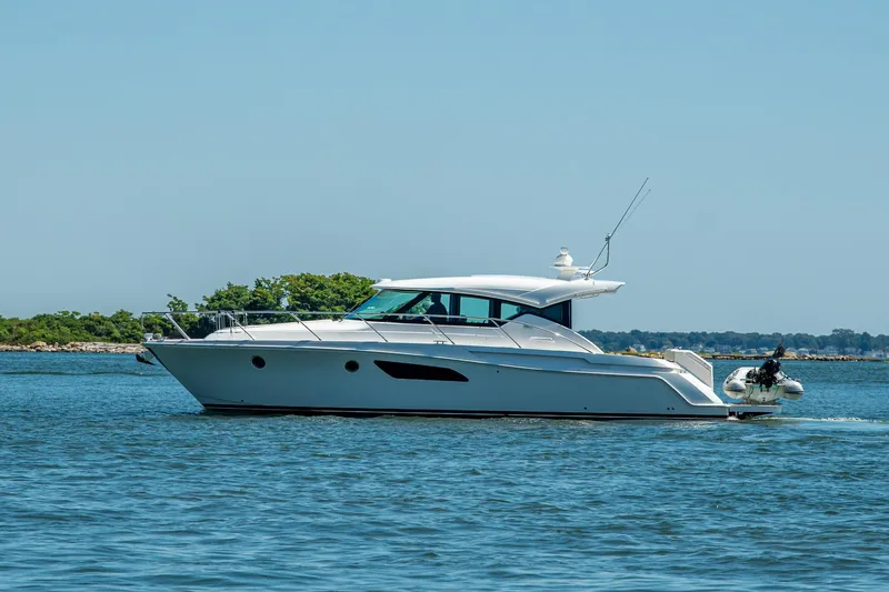 Slide: The Image of 2020 Tiara Yachts C44 Coupe cruising on calm waters near a lush shoreline. - 70