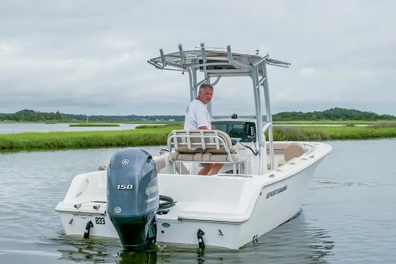 Slide: The Image of 2019 Sportsman Open 212 Center Console boat on calm water with lush green shoreline. - 2