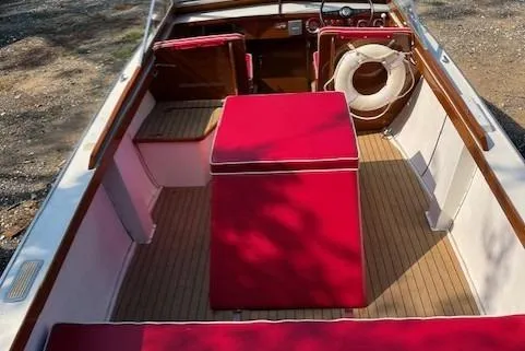 The Image of 1963 Chris-Craft Sea Skiff boat with red interior and wooden accents, parked outdoors. - 0