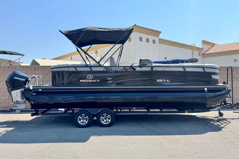 The Image of 2023 Regency 250 LE3 pontoon boat on trailer, featuring a Mercury outboard motor. - 0