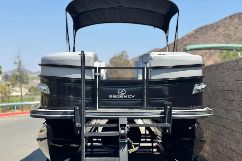 Slide: The Image of 2023 Regency 250 LE3 pontoon boat on trailer, black exterior, parked outdoors. - 2