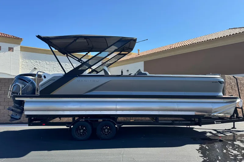 The Image of 2025 Manitou EXPLORE 26 pontoon boat on trailer, featuring sleek design and Yamaha engine. - 0