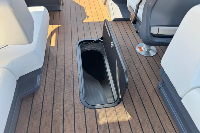 Slide: The Image of 2025 Manitou EXPLORE 26 boat interior with open storage compartment on deck. - 13