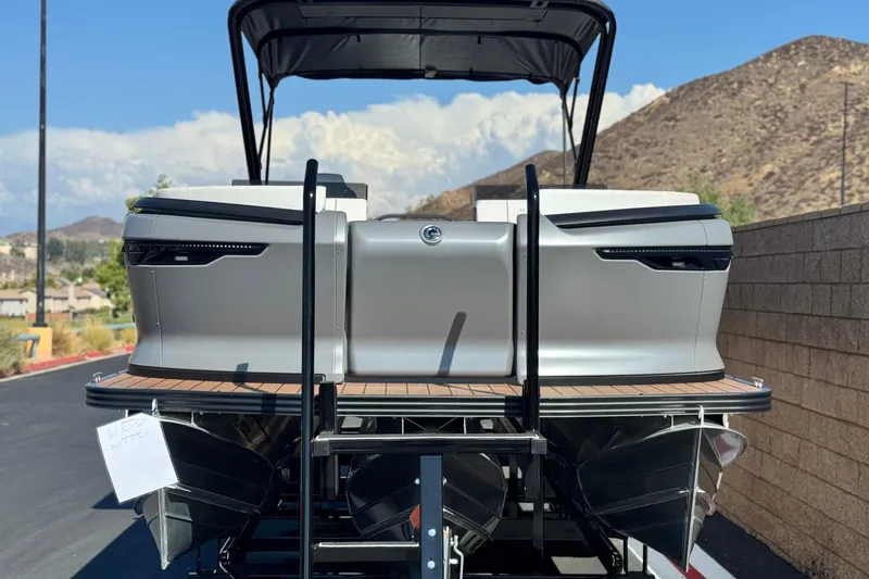 Slide: The Image of 2025 Manitou EXPLORE 26 pontoon boat, rear view, parked near mountains. - 2