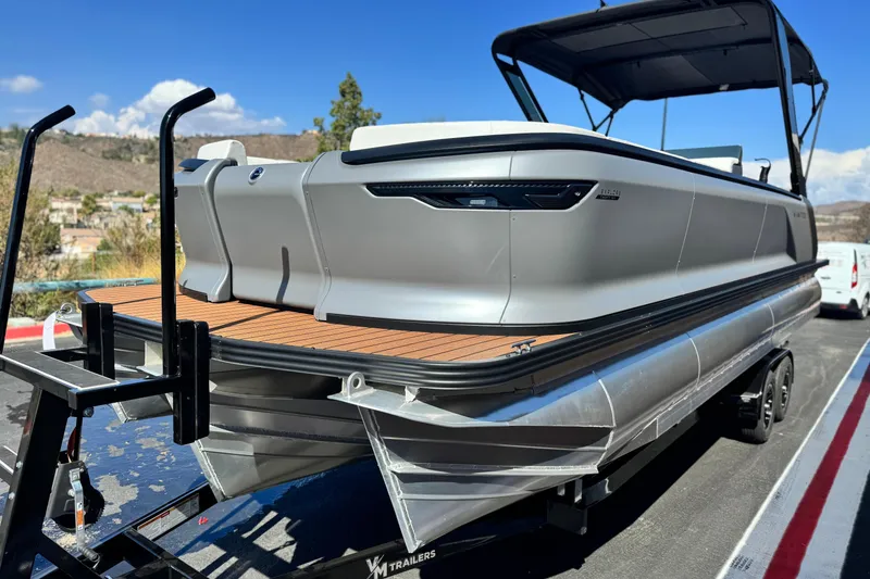 Slide: The Image of 2025 Manitou EXPLORE 26 pontoon boat on trailer, sleek design, outdoor setting. - 3