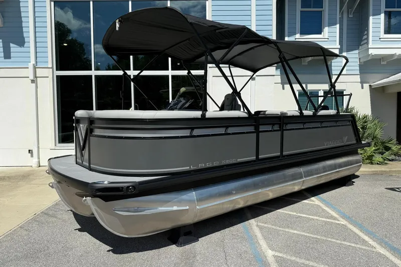 The Image of 2026 Viaggio Lago X-C pontoon boat with canopy, parked near a modern building. - 0
