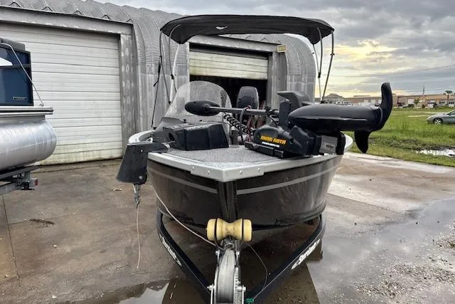 Slide: The Image of 2014 Alumacraft Escape 165 CS boat parked near a garage under cloudy skies. - 2
