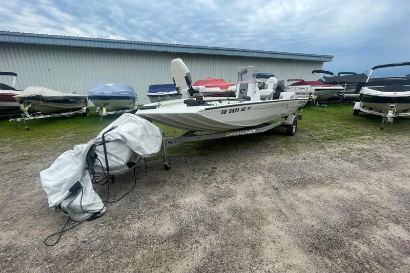 Slide: The Image of 2021 Crestliner 2000 Bay boat on trailer, parked outdoors near other covered boats. - 13