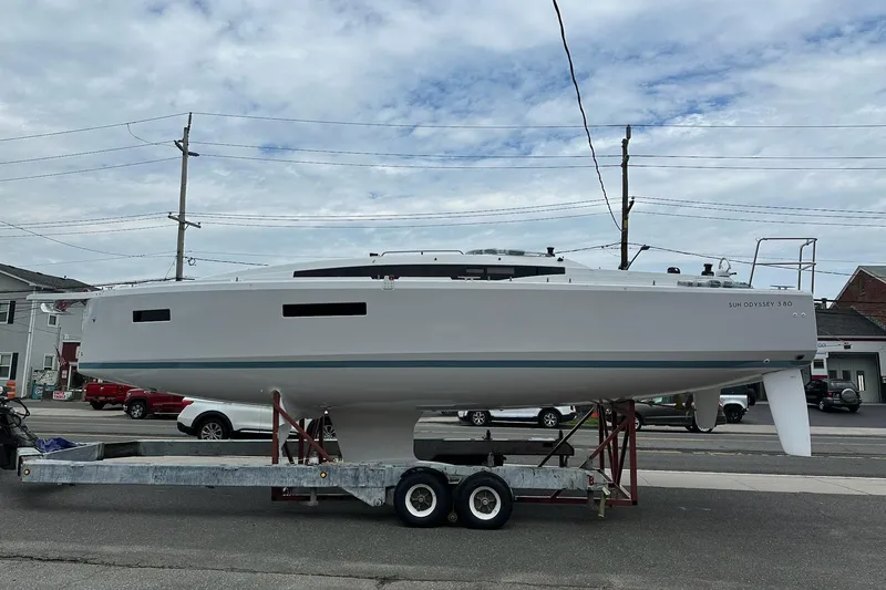 Slide: The Image of 2025 Jeanneau Sun Odyssey 380 sailboat on trailer, street background, cloudy sky. - 12