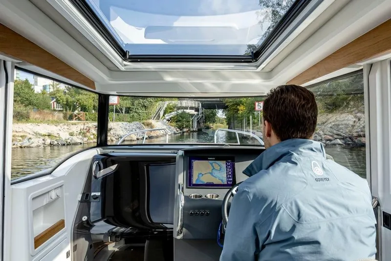 Slide: The Image of Man navigating a 2023 Nimbus C9-30 boat through a scenic waterway. - 6