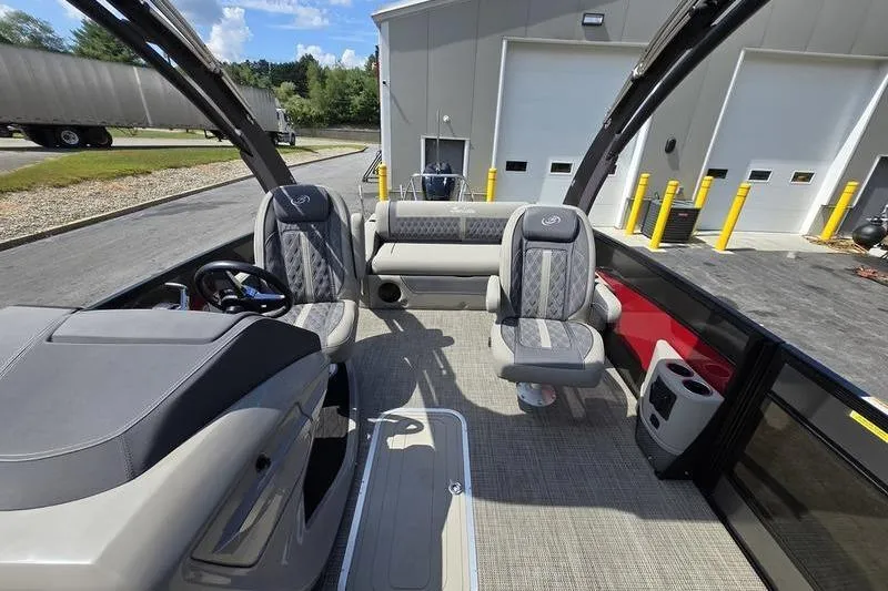 Slide: The Image of 2023 Barletta L25UCA pontoon boat interior with seating and helm, parked near a building. - 10