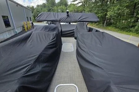 Slide: The Image of 2023 Barletta L25UCA pontoon boat covered, parked outdoors near trees and a building. - 3