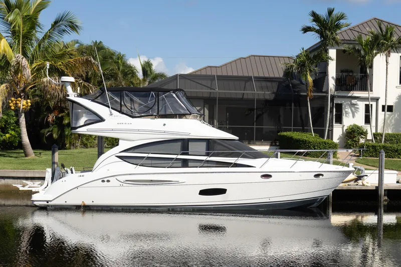 The Image of 2009 Meridian 391 Sedan yacht docked by a waterfront home, surrounded by palm trees. - 0