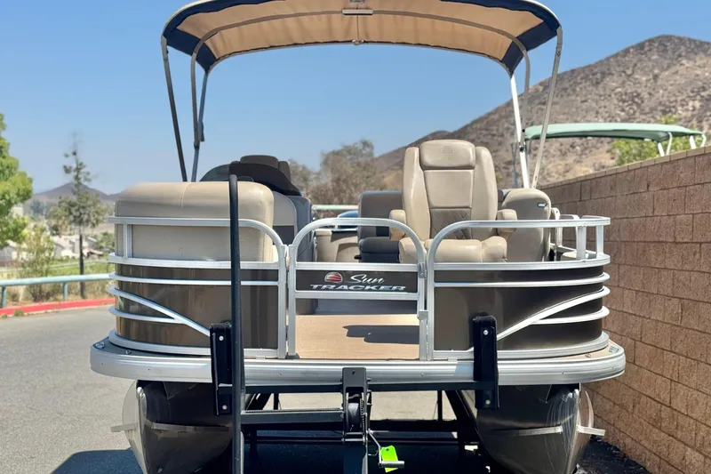 Slide: The Image of 2023 Sun Tracker SportFish 20 DLX pontoon boat with canopy, parked outdoors. - 2