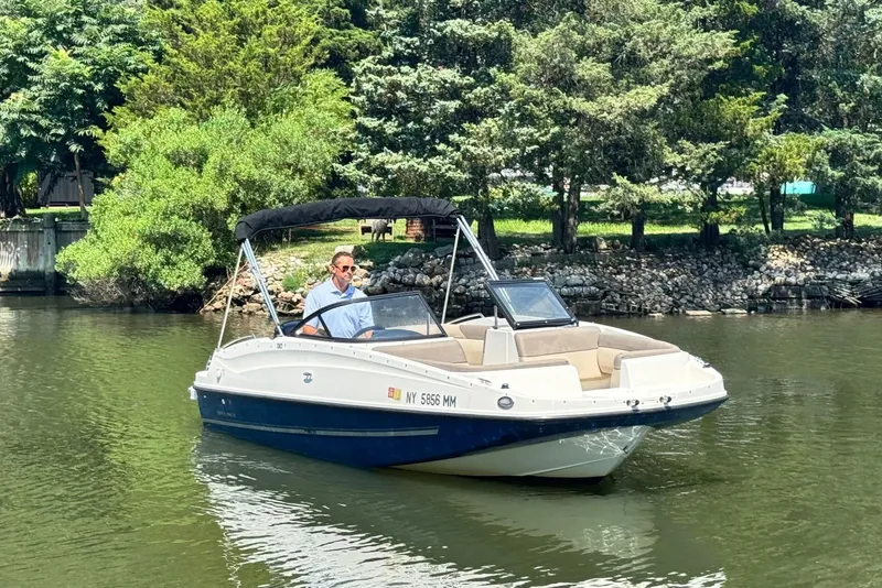 Slide: The Image of 2017 Bayliner 190 Deck Boat cruising on a calm river with lush greenery. - 1
