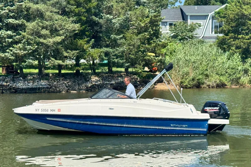 Slide: The Image of 2017 Bayliner 190 Deck Boat cruising on a scenic river with lush greenery. - 2