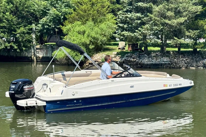 Slide: The Image of 2017 Bayliner 190 Deck Boat cruising on a calm river with lush greenery. - 4