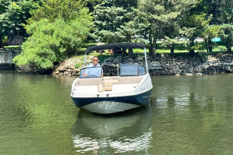Slide: The Image of 2017 Bayliner 190 Deck Boat on a calm lake with lush green trees. - 6