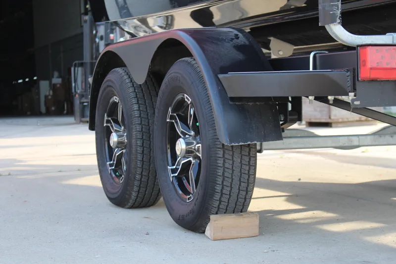 Slide: The Image of 2022 Chaparral 21 Surf trailer wheels on concrete, supported by a wooden block. - 18