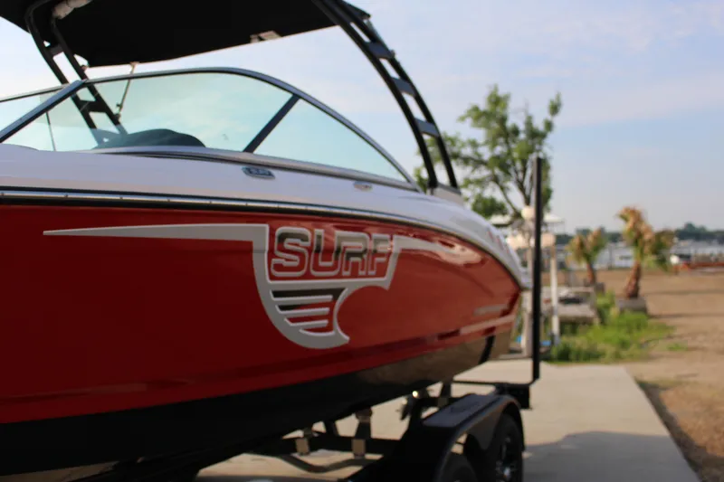 Slide: The Image of 2022 Chaparral 21 Surf boat in red, parked on a trailer near a waterfront. - 4