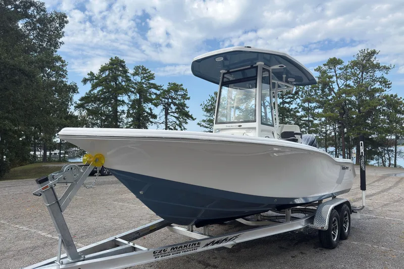 Slide: The Image of 2026 Tidewater 210 CC Adventure boat on trailer, parked near trees under a cloudy sky. - 2