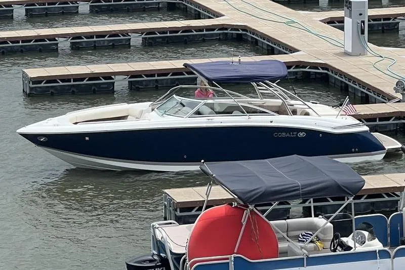 Slide: The Image of 2009 Cobalt 296 boat on a lake, surrounded by trees under a clear blue sky. - 2