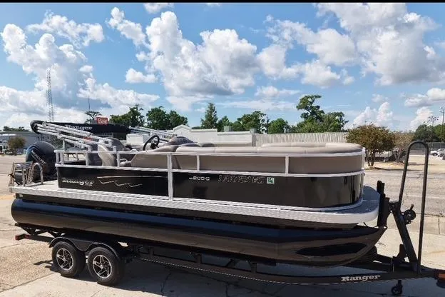 The Image of 2024 Ranger RP200C pontoon boat on trailer under a blue sky with clouds. - 0