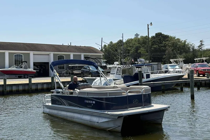 Slide: The Image of 2018 Avalon GS 2185 CR pontoon boat docked near marina with various boats and vehicles. - 5