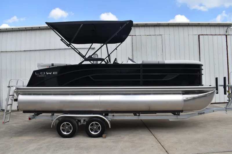 The Image of 2026 Lowe SS 210 pontoon boat on trailer, black exterior, parked by a metal building. - 0