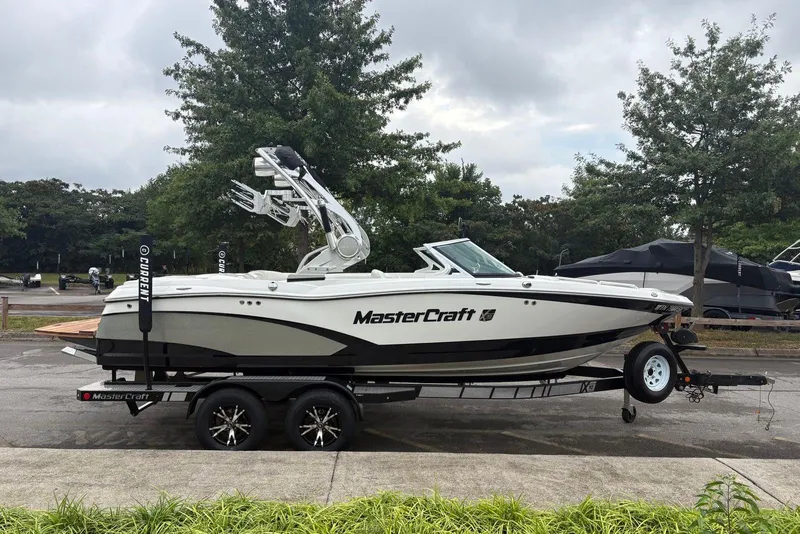 Slide: The Image of 2014 MasterCraft X10 boat on trailer, parked outdoors with trees in background. - 2