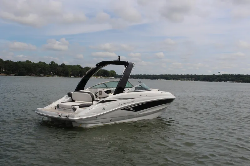Slide: The Image of 2023 Crownline E235 boat on a calm lake under a partly cloudy sky. - 0