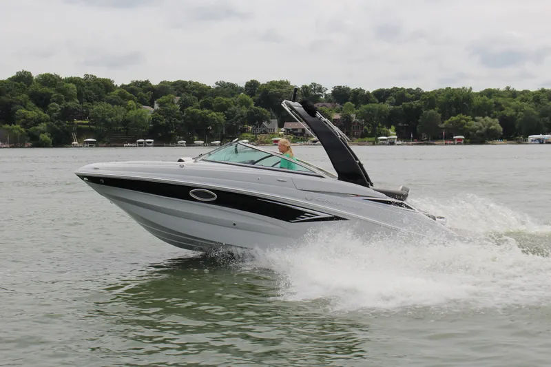 Slide: The Image of 2023 Crownline E235 boat cruising on a lake with lush green shoreline. - 17