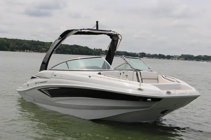 Slide: The Image of 2023 Crownline E235 boat on a calm lake with lush green shoreline. - 18