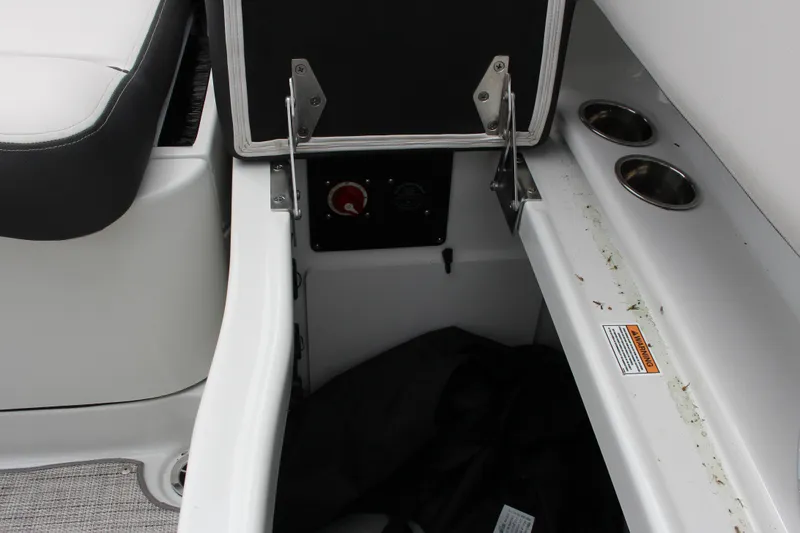 Slide: The Image of 2023 Crownline E235 boat storage compartment with cup holders and safety warning label. - 3