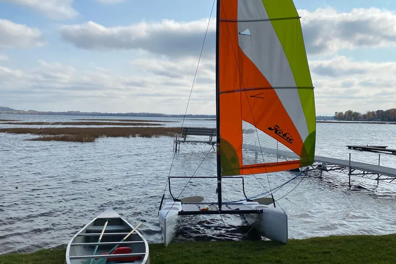 Slide: The Image of 2019 Hobie Cat Wave 13 sailboat by a lake with a colorful sail. - 2
