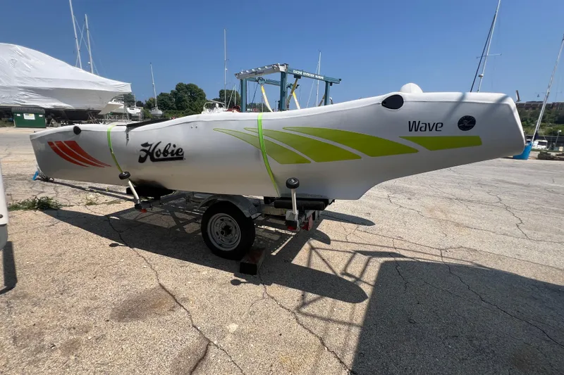 Slide: The Image of 2019 Hobie Cat Wave 13 sailboat on trailer, vibrant graphics, marina background. - 4