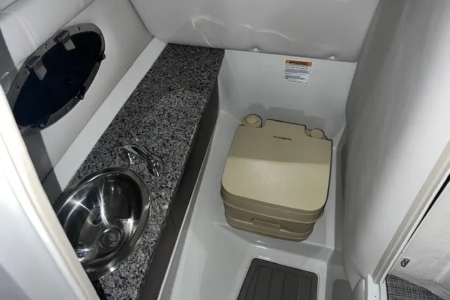 Slide: The Image of 2023 Crownline E255 boat interior with compact bathroom, featuring a sink and portable toilet. - 3