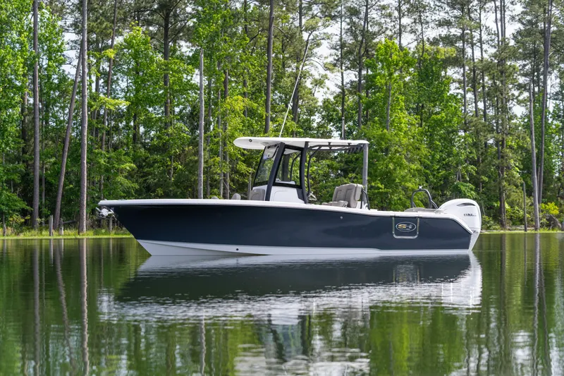 Slide: The Image of 2026 Sea Hunt Ultra 255 SE boat on calm water, surrounded by lush green trees. - 12