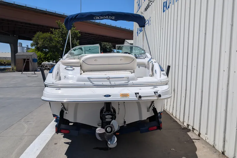 Slide: The Image of 2006 Crownline 240 EX boat with blue canopy, parked near a white building. - 2