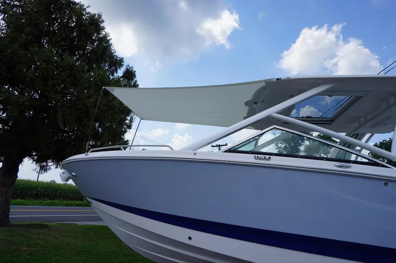 Slide: The Image of 2025 Chaparral 280 OSX boat with canopy, parked near a tree under a blue sky. - 52