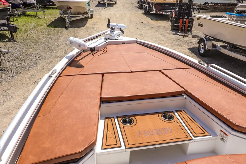 Slide: The Image of 2026 Avid 23 Fusion boat with brown deck cushions and cup holders, parked on gravel. - 17