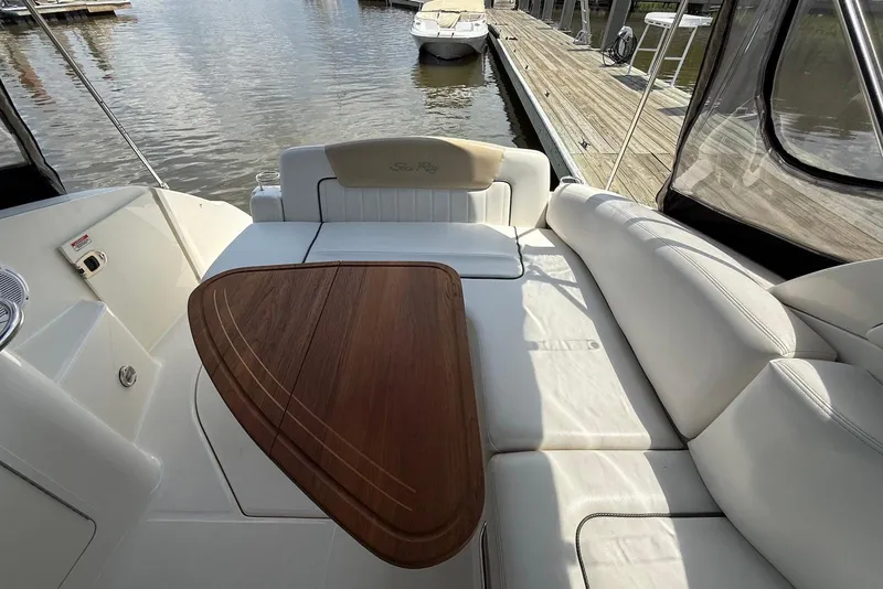 Slide: The Image of 2009 Sea Ray 270 Sundancer boat interior with white seating and wooden table, docked at marina. - 16