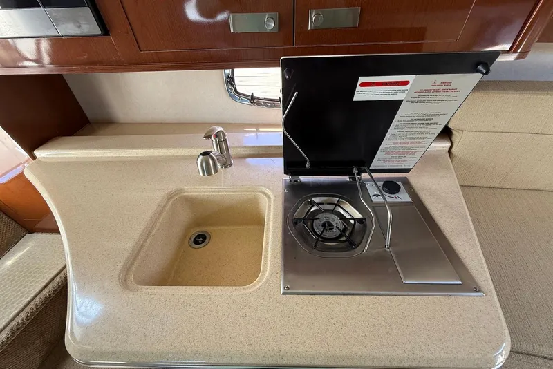 Slide: The Image of 2009 Sea Ray 270 Sundancer galley with sink and stove, featuring wood cabinetry. - 22