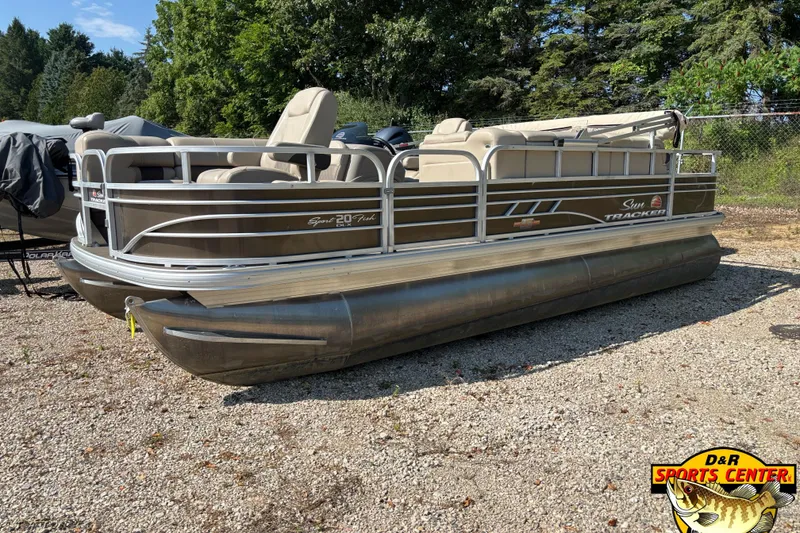 The Image of 2023 Sun Tracker SportFish 20 DLX pontoon boat on gravel lot, surrounded by trees. - 0